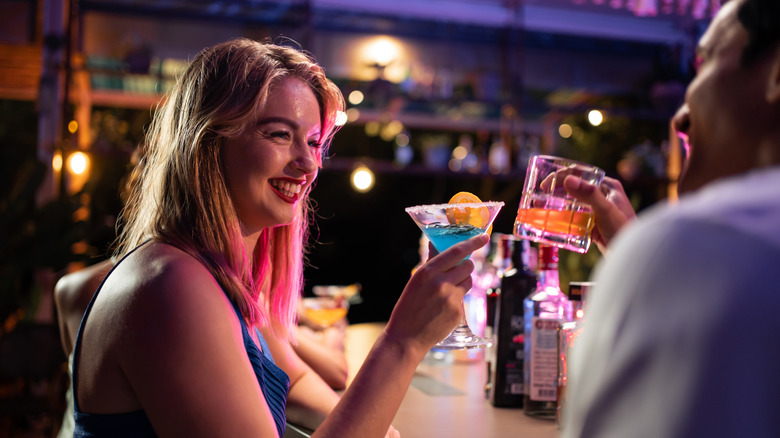 A young woman holding a martini toasts with a man holding a drink