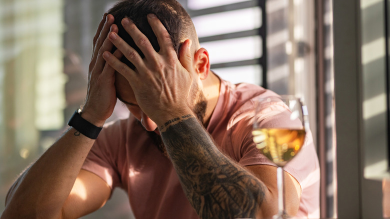 A man holding his head in his hands next to a glass of wine