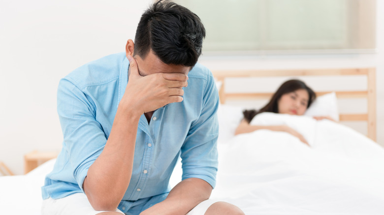 A man sitting at the edge of the bed hiding his face with his hand