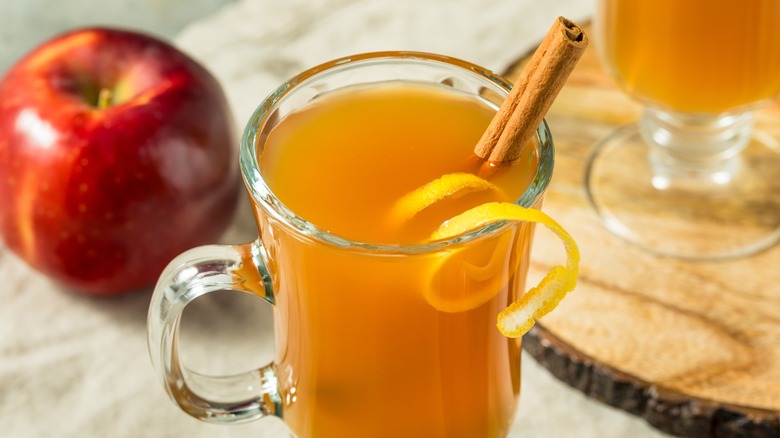 A glass mug of hot apple cider next to an apple