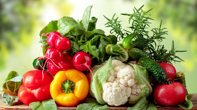 An outdoor table with tomatoes, bell peppers, cauliflower, and greens