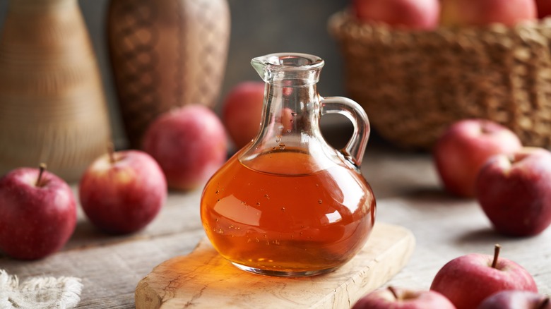 glass container of apple cider vinegar surrounded by apples