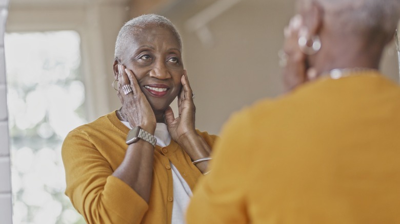 older woman smiling in the mirror while touching her face