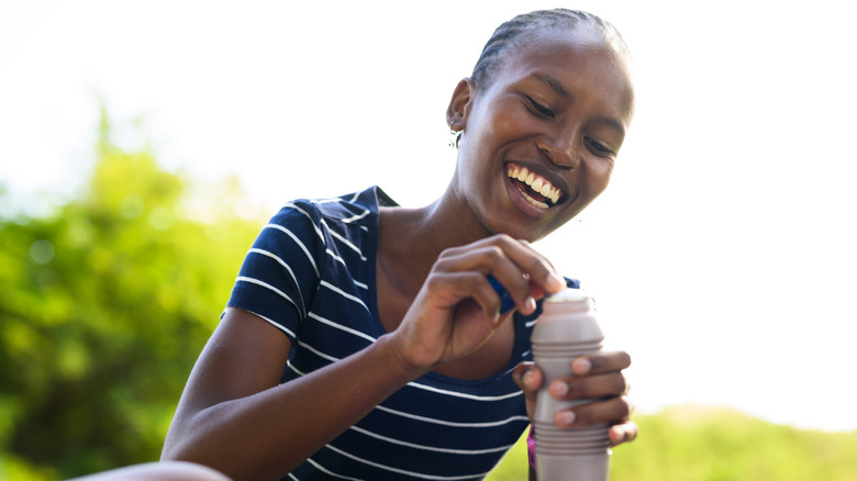 A smiling young woman opening chocolate milk outside