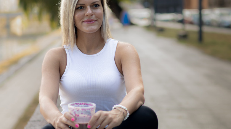 A woman holding chocolate milk while on a park bench