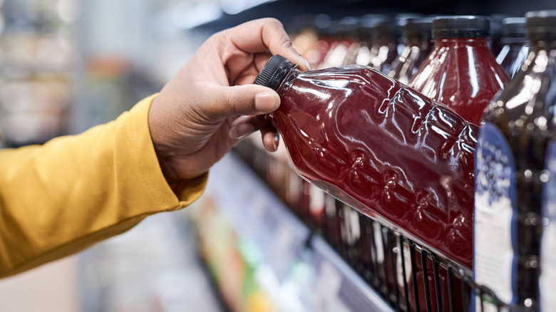 hand grabbing bottle of red drink from shelf