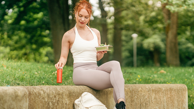 woman in athletic gear eating salad and drinking juice