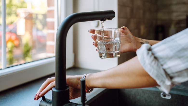 A woman's hand filling a glass with filtered water