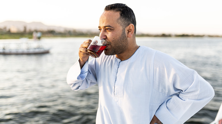 man drinking dark red juice from a glass outside