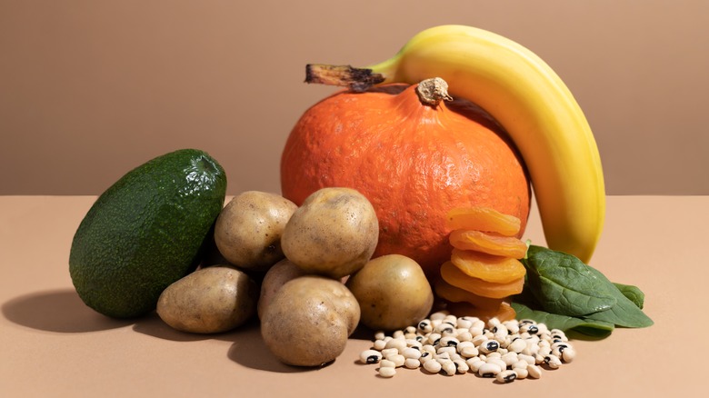 An avocado, pumpkin, banana, beans, potatoes, and spinach on a table to show potassium-rich foods