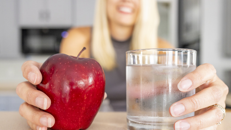 woman holding apple and glass of water in kitchen