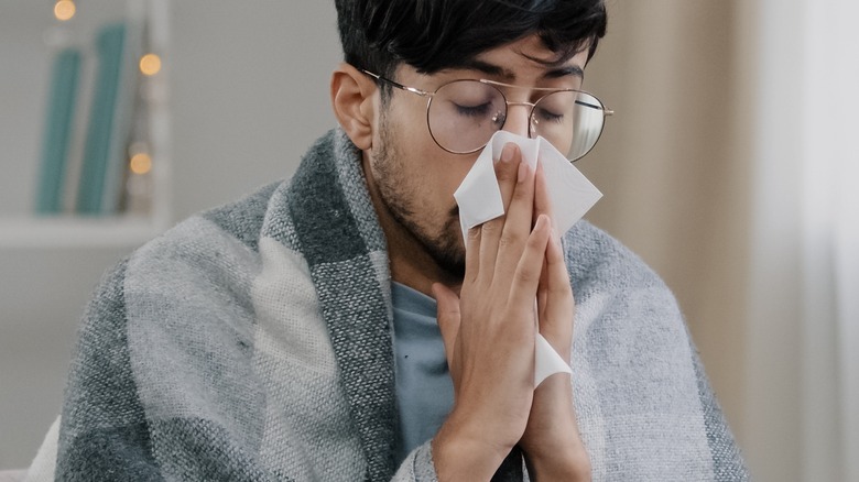 man wrapped in blanket blowing nose
