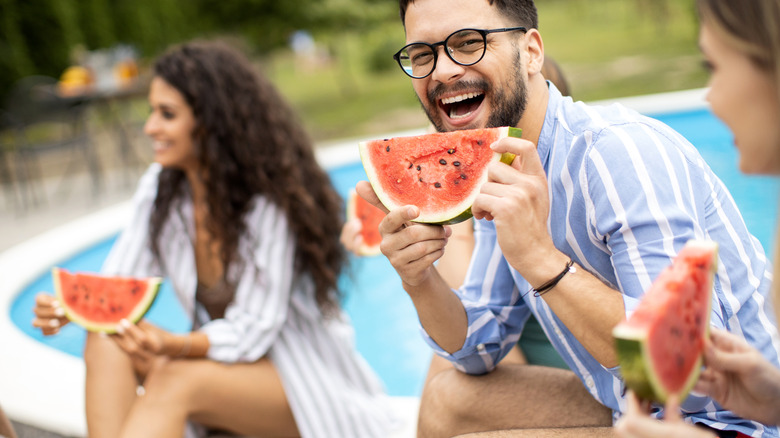 Smiling friends eating watermelon by pool