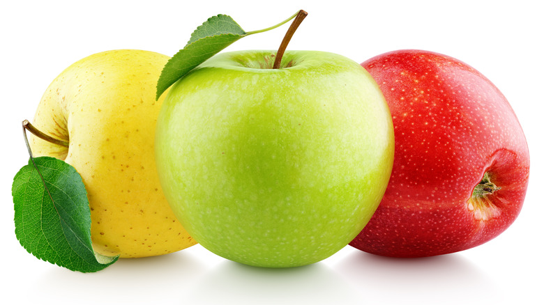 A green apple between a yellow apple and a red apple against a white background