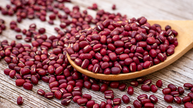 Close up of a wooden spoon filled with azuki beans on a piece of wood covered with azuki beans