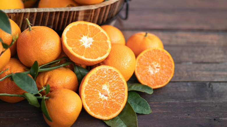 Halved and whole oranges on wood next to a bowl of oranges