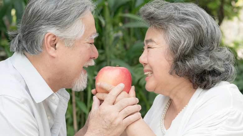 older male and female couple smiling with apple