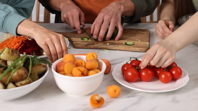 The hands of several people cutting fruit and vegetables