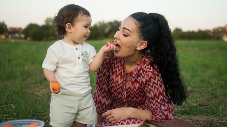 toddler feeding mom apricot during picnic outside