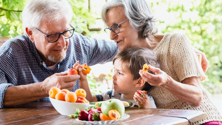 older couple with young child eating apricots at table