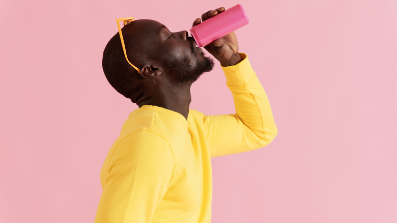 man drinking pink can of soda