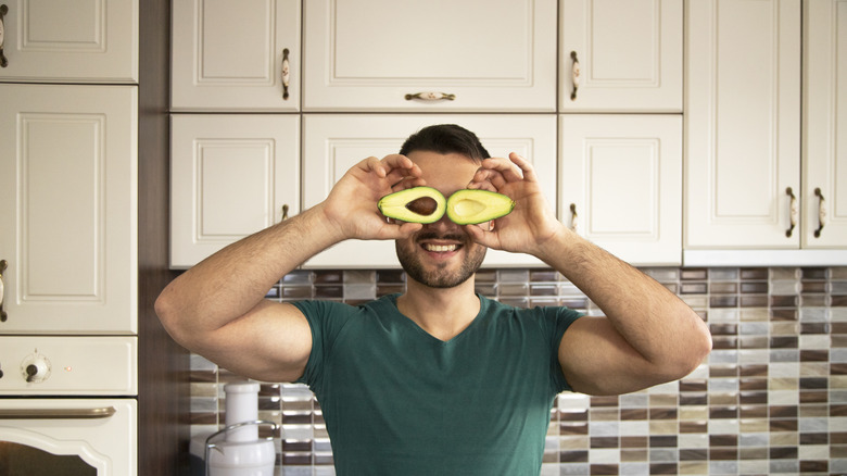 man holding sliced avocado over his eyes