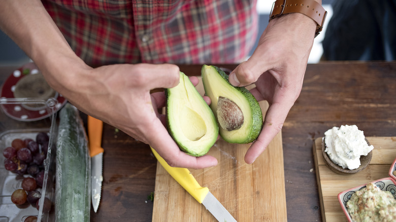 man's hands holding a sliced avocado