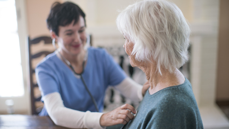 senior woman having heart checked by nurse at home