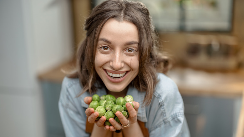 smiling woman holding handful of Brussels sprouts