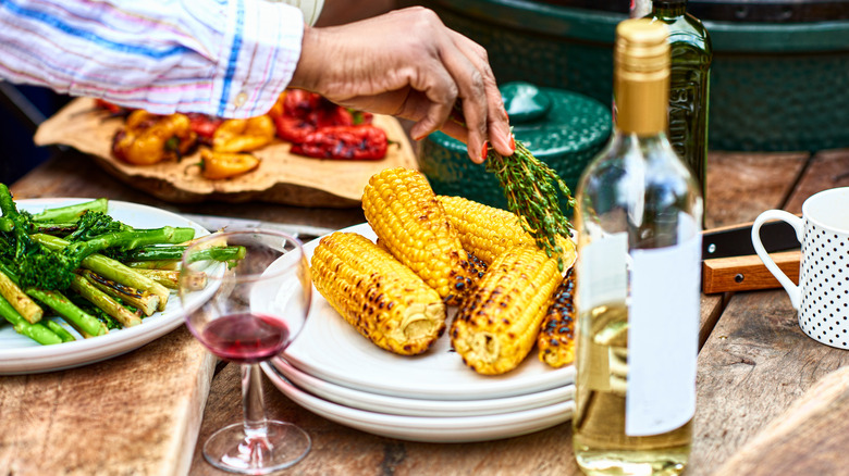 Grilled corn on a plate next to plates of other vegetables