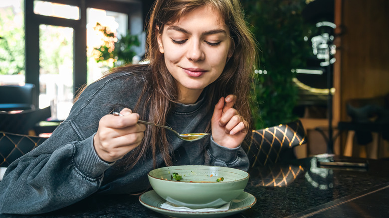 A young woman eating a bowl of soup