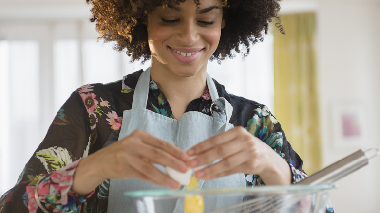 A smiling young woman cracking an egg in a bowl