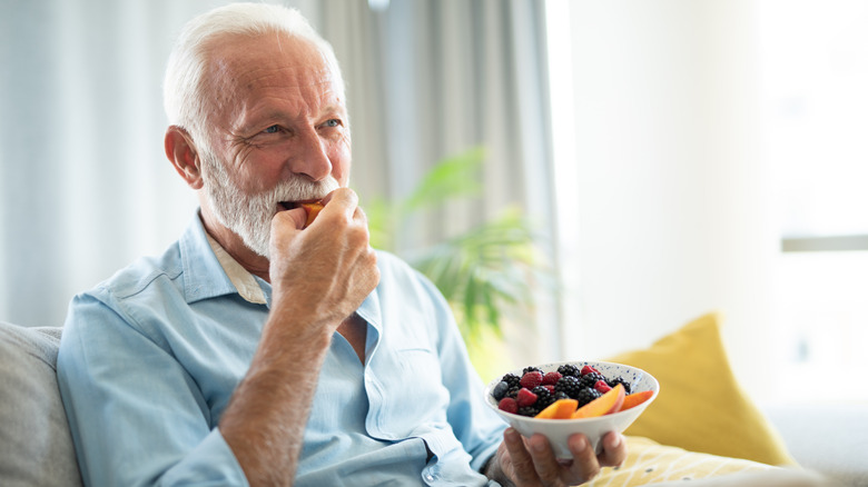 older man eating fruit salad on couch