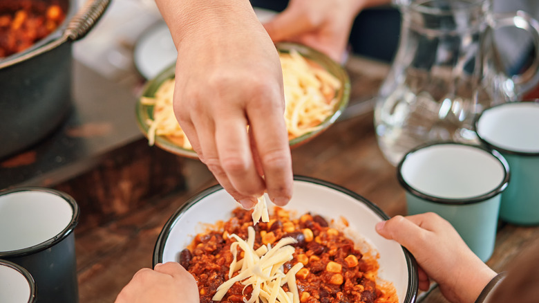 woman adding cheese to bean dish of chili