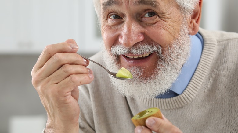 happy senior man eating kiwi fruit