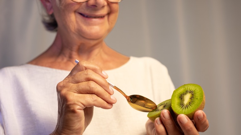Smiling woman eating kiwifruit