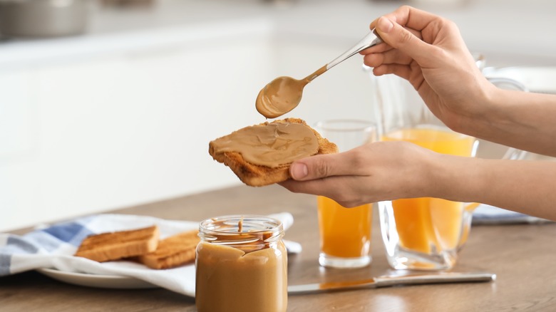 woman's hand spooning peanut butter on toast