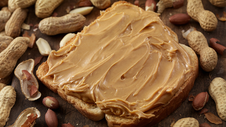 Slice of peanut butter toast surrounded by peanuts