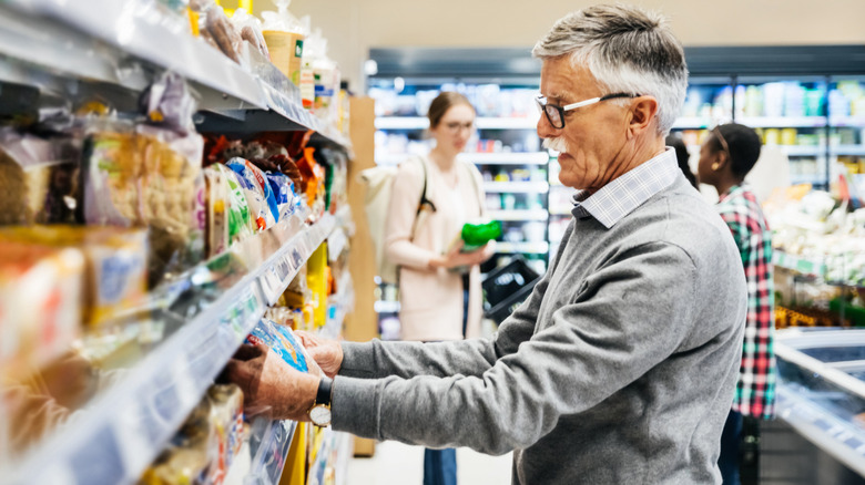 older man looking at bread label in grocery store