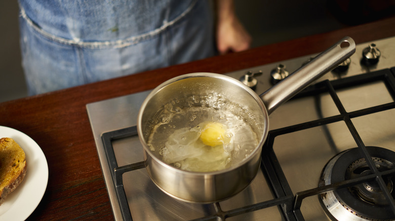 person cooking poached eggs in sauce pan