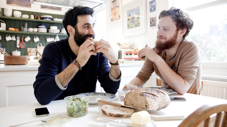 two smiling men eating bread in kitchen