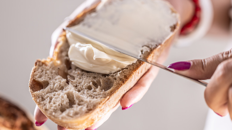 A woman's hands spreading butter on sourdough bread slice