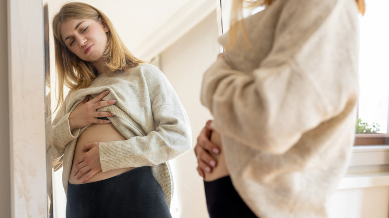 woman unhappy about belly fat looking in mirror