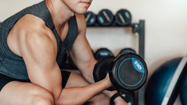 man seated on gym bench lifting a free weight