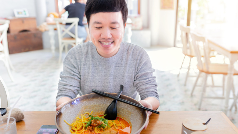 smiling man holding bowl of curry soup