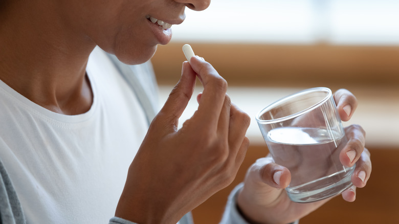 Woman holding a glass of water and taking a pill