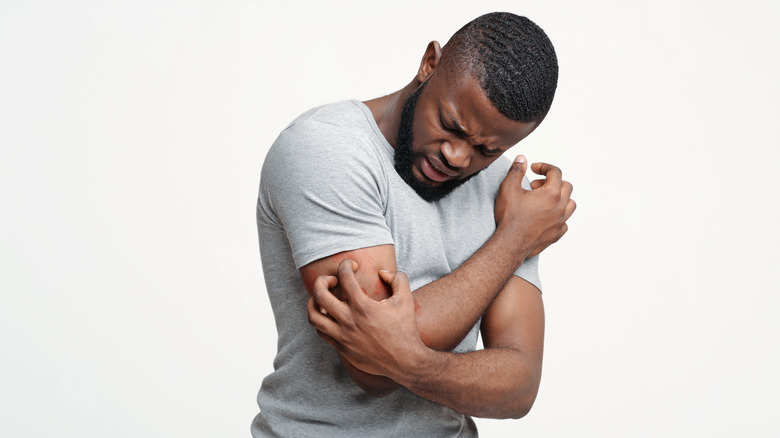 Black man itching a rash on his arm