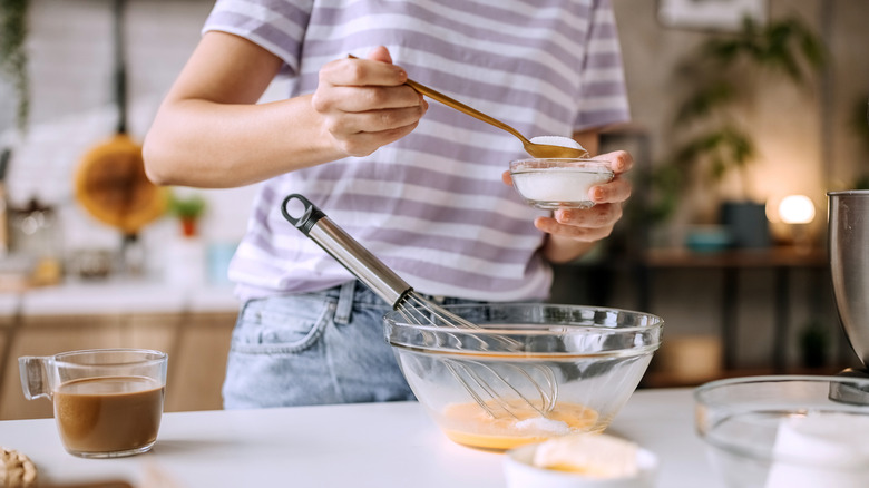 person adding sugar to a bowl of eggs