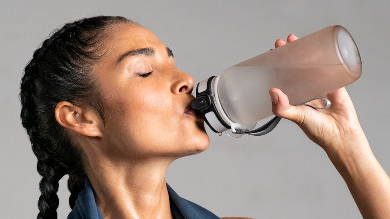 woman with two braids drinking water before a workout