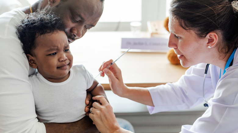 toddler getting vaccine while dad holds him